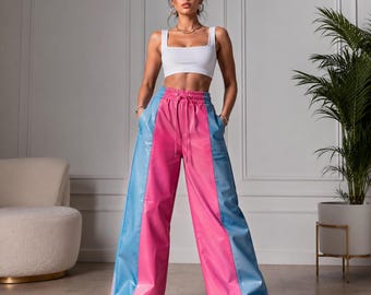 Op de afbeelding: Een witte mouwloze crop top met een vierkante halslijn gecombineerd met een wijde broek met een color-block ontwerp. De broek heeft een felroze middenpaneel en lichtblauwe zijpanelen, een elastische tailleband met trekkoord en zakken.