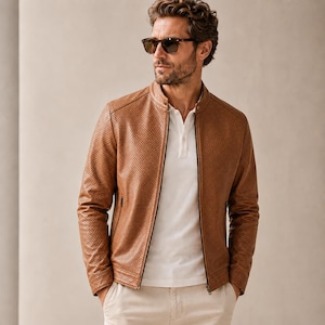May include: A tan perforated leather jacket with a mandarin collar and a full-length front zipper, worn over a white polo shirt and light-colored trousers. The jacket features a textured, dotted pattern across the surface and long sleeves.