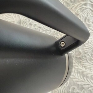 May include: Close-up of a black insulated water bottle with a curved handle. The bottle has a matte finish and a silver band near the base. The handle is attached with a small metal screw.