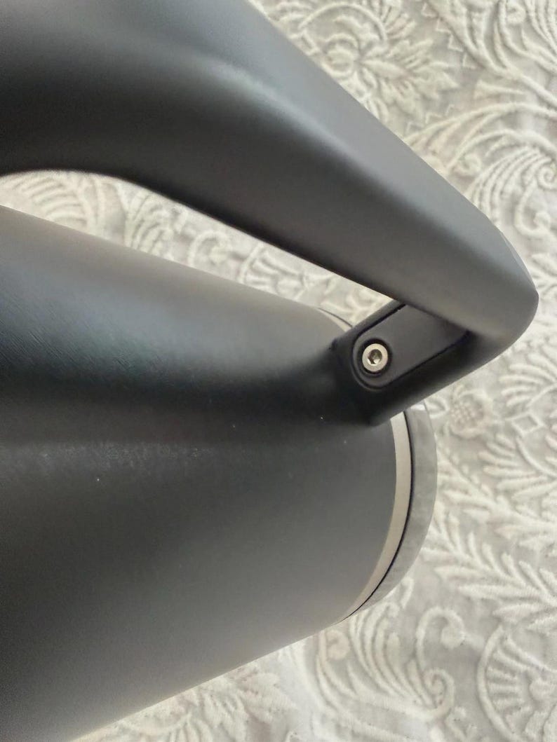 May include: Close-up of a black insulated water bottle with a curved handle. The bottle has a matte finish and a silver band near the base. The handle is attached with a small metal screw.