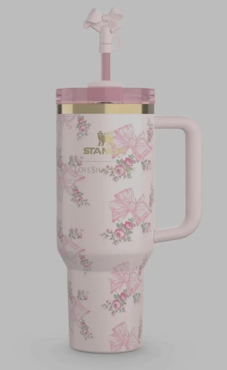 May include: A pink insulated travel mug with a handle, lid, and straw. The mug is adorned with pink bows and roses. A gold band accents the top. The text "STANLEY" and "LOVESHAPE" are printed on the mug.