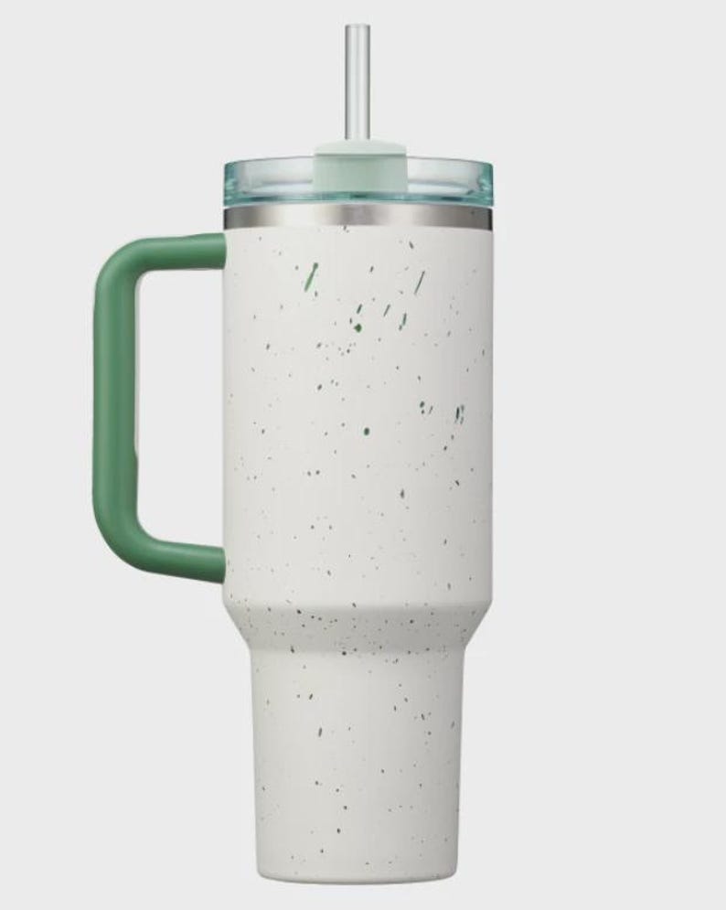 May include: A white stainless steel tumbler with a speckled pattern in dark green. The cup features a large, solid dark green handle on the side, a clear plastic lid, and a matching clear straw inserted through the center of the lid.