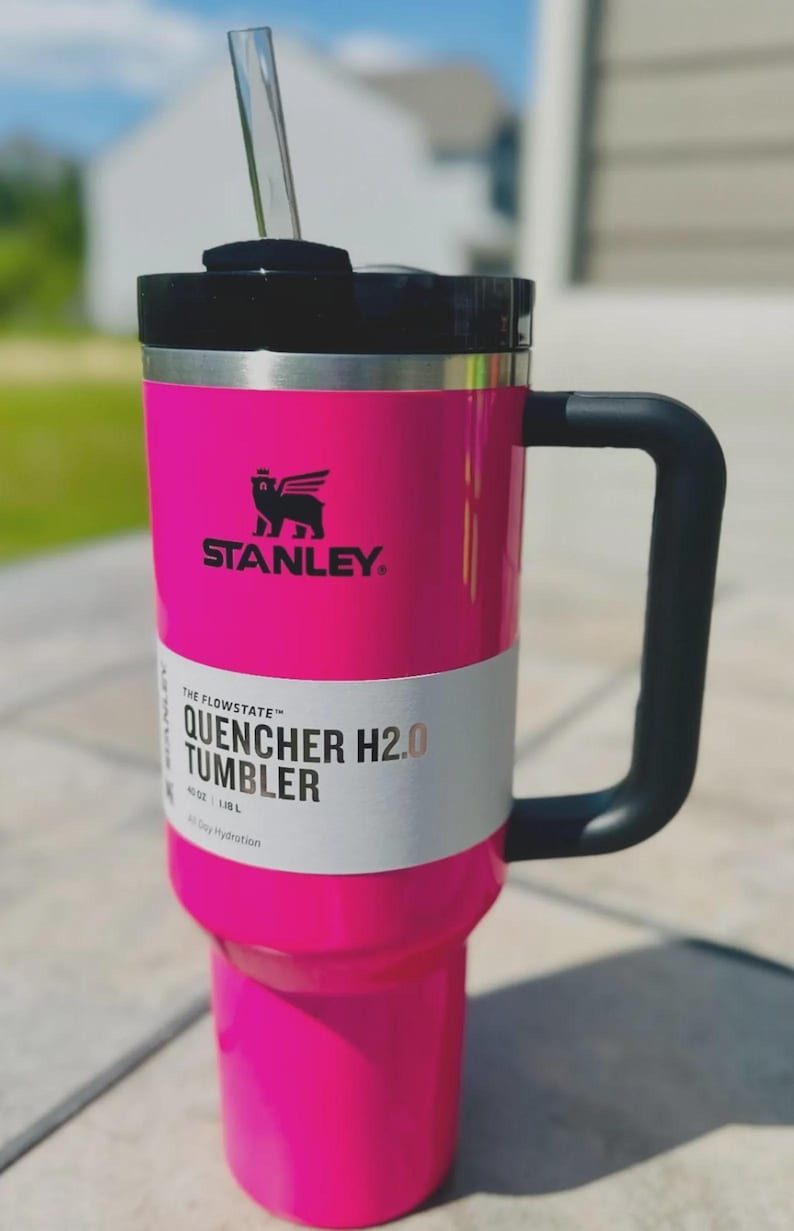 Op de afbeelding: Een felroze Stanley Quencher H2.0 Tumbler met een zwarte handgreep en deksel. De beker heeft een rietje en een wit label met de tekst "QUENCHER H2.0 TUMBLER". Het Stanley-logo is zichtbaar.