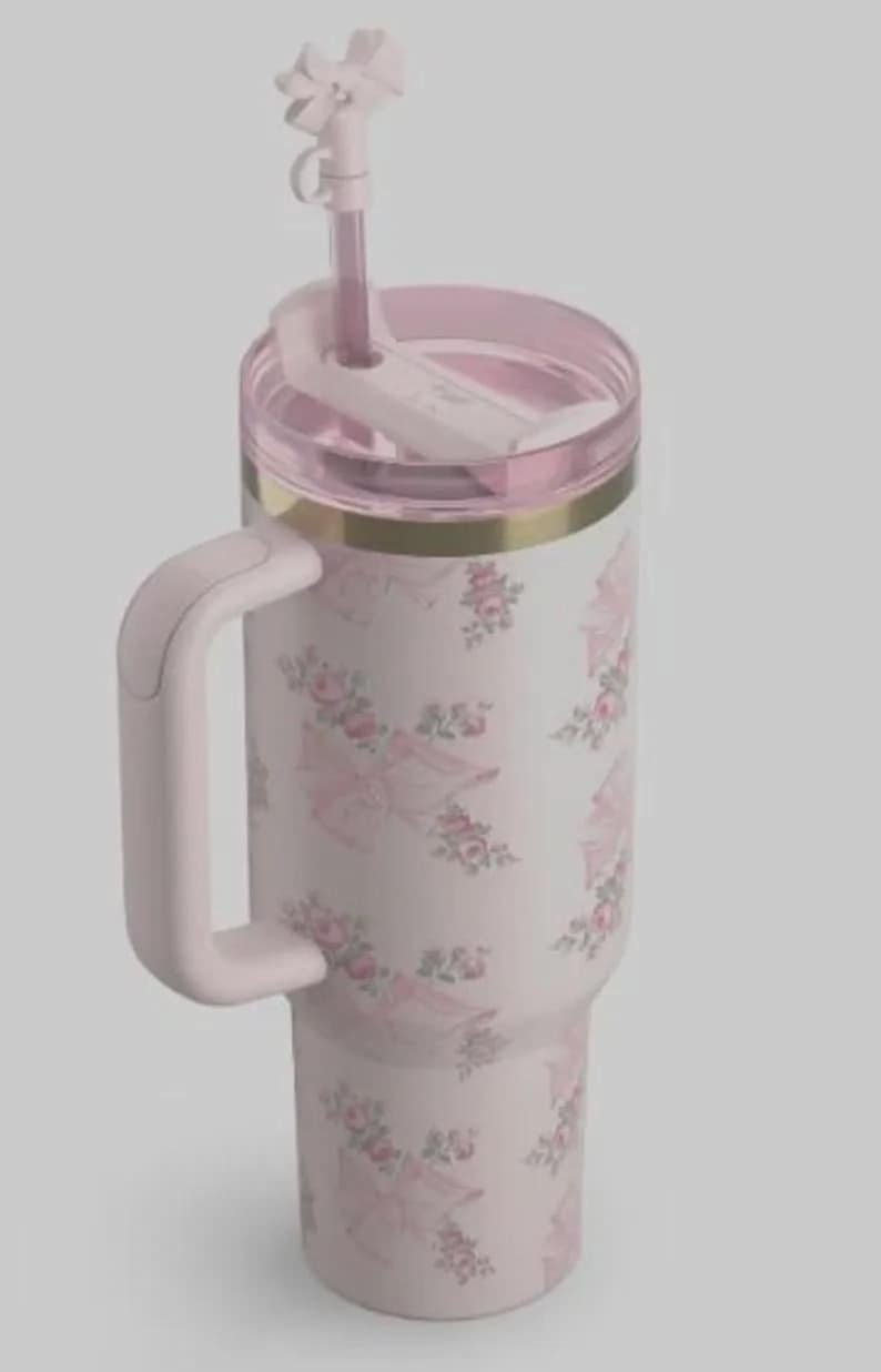 May include: A light pink insulated tumbler with a handle, straw, and lid. The tumbler features a floral and umbrella pattern in pink and white. A gold band accents the top.