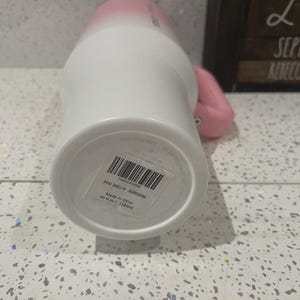 May include: A white and pink ombre tumbler with a handle, featuring a sticker on the base with a barcode, the text PHI SKU # 3000696, and the capacity of 40 fl oz / 1183 ml. The tumbler has a cylindrical body and a sturdy side handle.