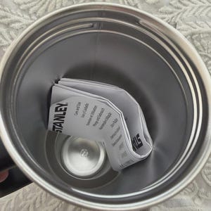 May include: Stainless steel Stanley tumbler interior with a folded instruction manual. The manual is white with black text and the Stanley logo. The tumbler has a silver finish.