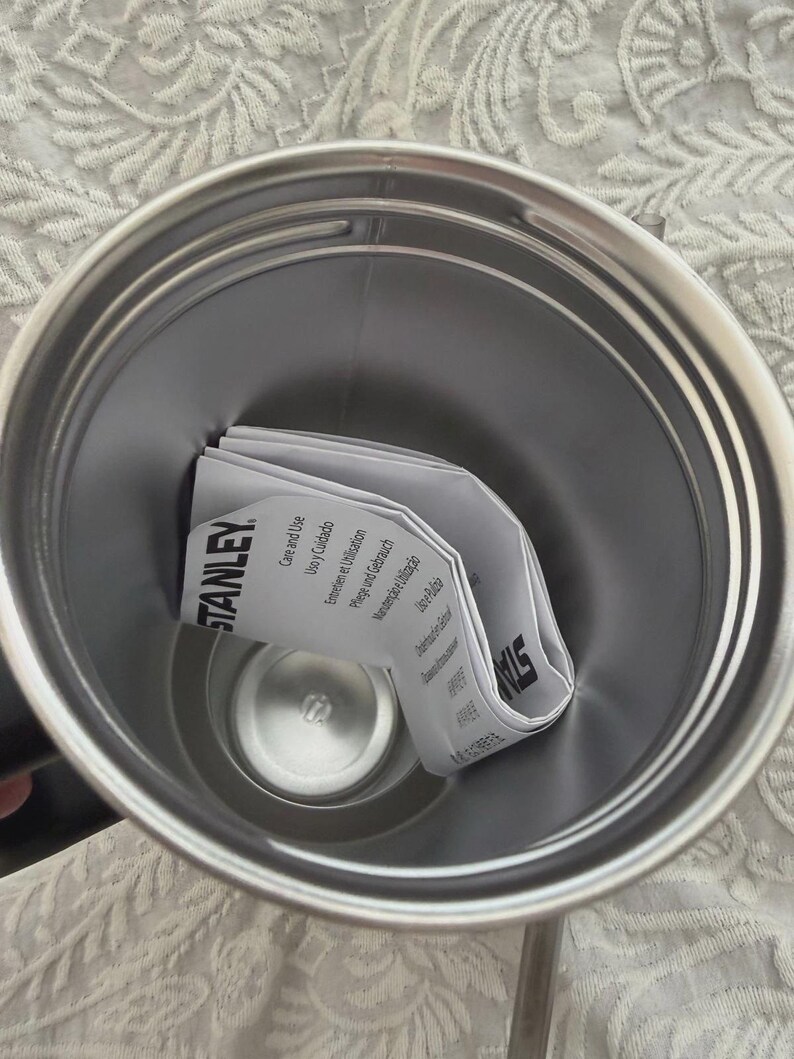 May include: Stainless steel Stanley tumbler interior with a folded instruction manual. The manual is white with black text and the Stanley logo. The tumbler has a silver finish.