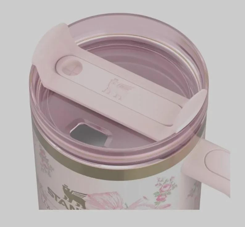 May include: A close-up of a pink and white floral Stanley tumbler with a matching pink lid. The lid has a sliding closure and the Stanley logo is visible. The tumbler has a gold band near the top and floral designs.