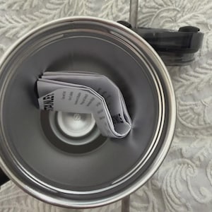 May include: A stainless steel Stanley tumbler with a black lid and a clear straw. The interior of the tumbler contains a folded instruction manual. The tumbler is silver and has a double-walled design.