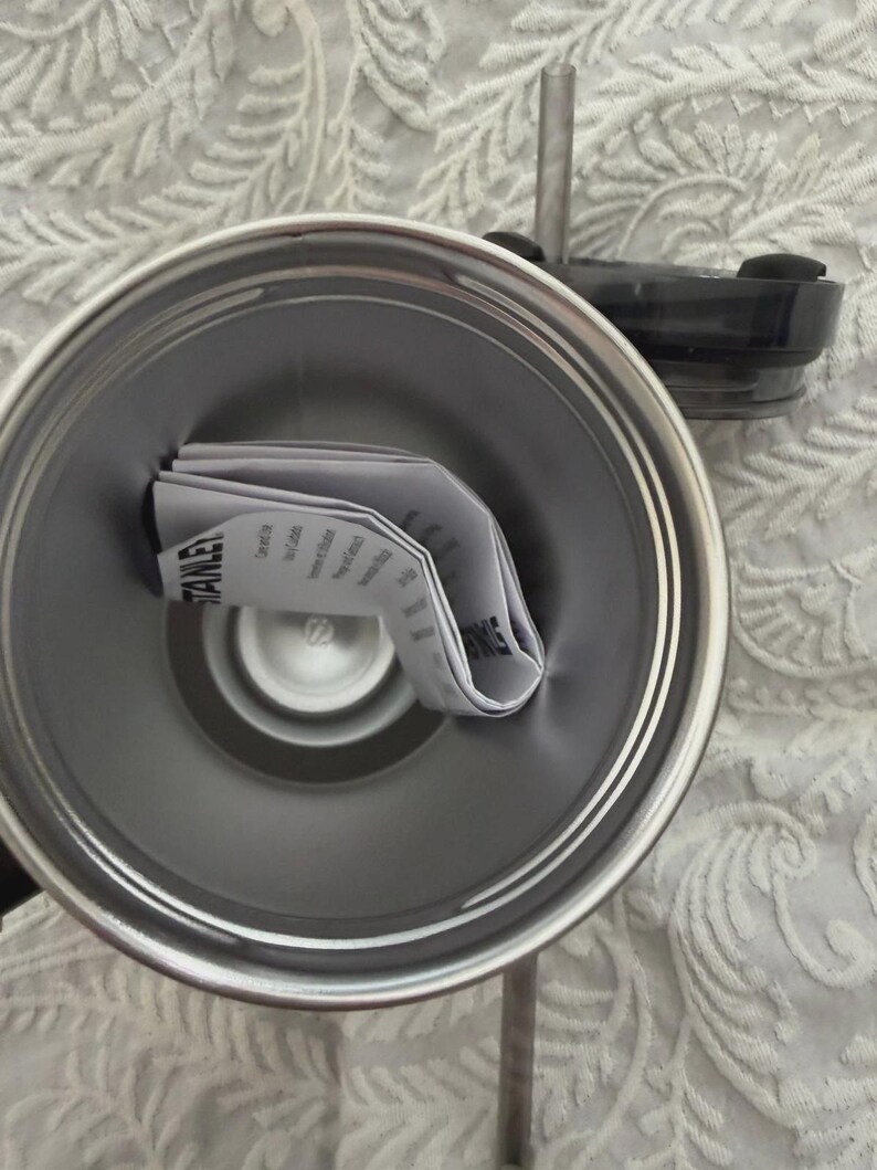 May include: A stainless steel Stanley tumbler with a black lid and a clear straw. The interior of the tumbler contains a folded instruction manual. The tumbler is silver and has a double-walled design.