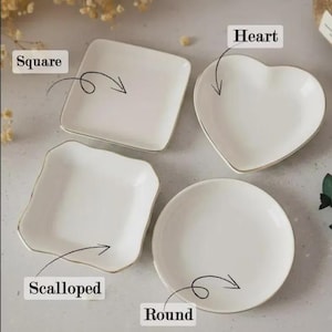 Op de afbeelding: Vier witte keramische schaaltjes in verschillende vormen: vierkant, hartvormig, geschulpt en rond. Elk schaaltje heeft een gouden rand. De vormen zijn gelabeld met de woorden "Square", "Heart", "Scalloped" en "Round".