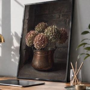 May include: A framed wall art print titled DIGITAL TREASURY PRINTS featuring a still life painting of dried hydrangea flowers in a weathered copper pot set against a dark brick background, displayed in a simple black frame on a wooden desk.