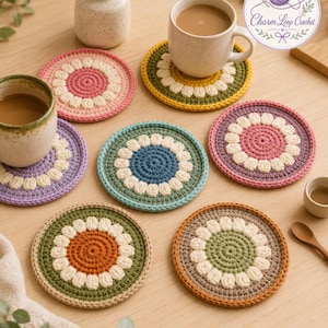 May include: A collection of six circular crochet coasters featuring a central solid color, a ring of cream-colored petals, and a contrasting outer border. The coasters are displayed in various color combinations including pink, green, blue, purple, and orange.