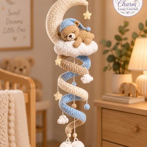 May include: A crochet mobile featuring a beige crescent moon, a brown bear wearing a blue nightcap resting on a white cloud, and a spiral structure in alternating blue and beige yarn. Small yellow stars, white clouds, and white pom-poms hang below.