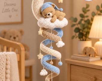 May include: A crochet mobile featuring a beige crescent moon, a brown bear wearing a blue nightcap resting on a white cloud, and a spiral structure in alternating blue and beige yarn. Small yellow stars, white clouds, and white pom-poms hang below.