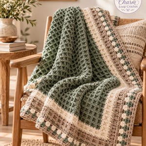 May include: A crochet blanket featuring a sage green waffle stitch center bordered by cream and beige stripes with a small floral motif. The blanket is draped over a wooden chair and includes a logo reading Charm Loop Crochet.