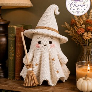 May include: A cream-colored crocheted ghost figurine wearing a pointed witch hat with a tan band. The ghost features embroidered black eyes, a small smile, pink cheeks, and three small gold stars. It holds a miniature wooden broom with tan bristles.
