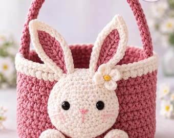 May include: A round, dusty rose crochet basket featuring a white bunny face on the front with black eyes, a pink nose, and two long ears. The basket has a sturdy handle and a small white flower accent. The text Charm Loop Crochet is visible.
