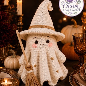 May include: A cream-colored crocheted ghost figurine wearing a pointed hat with a tan band. The ghost has black eyes, a small smile, and pink cheeks, with small gold star accents on its body. It holds a miniature wooden broom with tan bristles.