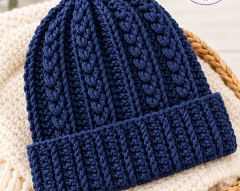 May include: A dark blue crochet beanie featuring a vertical cable knit pattern and a wide ribbed brim. The hat is topped with a circular logo that reads Charm Loop Crochet with an illustration of a ball of yarn and a crochet hook.
