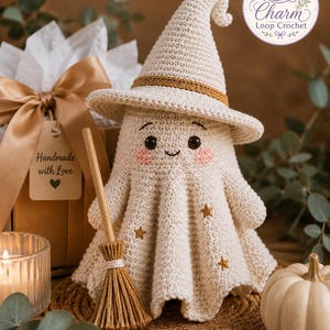 May include: A cream-colored crocheted ghost figurine wearing a matching pointed witch hat with a gold band. The ghost features embroidered black eyes, a small smile, pink cheeks, and gold star accents. A small wooden broomstick stands beside it.