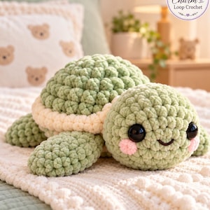 Op de afbeelding: Een gehaakt schildpadknuffeltje gemaakt van zacht saliegroen garen met een crèmekleurige rand om het schild. De schildpad heeft grote zwarte veiligheidsogen, een geborduurde glimlach en kleine roze ronde wangen. Het logo Charm Loop Crochet is zichtbaar.