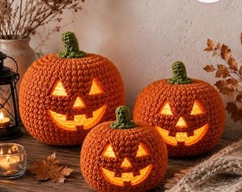 May include: Three orange crocheted pumpkins with green stems and carved jack-o'-lantern faces. Each pumpkin is illuminated from within, casting a warm glow through the triangular eyes, noses, and jagged mouths. The texture is yarn-based.