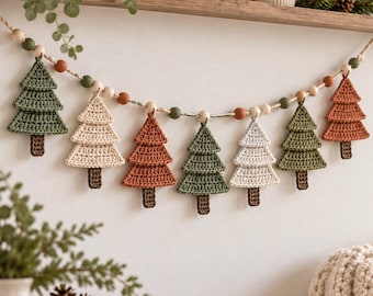 May include: A crochet garland featuring alternating pine tree shapes in sage green, cream, and terracotta colors, each with a brown trunk. The trees are strung on a cord interspersed with round wooden beads in natural, green, and rust tones.