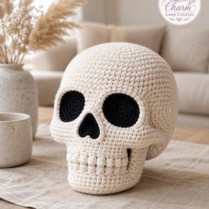 May include: A cream-colored crocheted skull with deep black eye sockets and a black nasal cavity. The skull features a textured surface created by individual yarn stitches, with a row of rounded, bobble-like stitches forming the teeth.