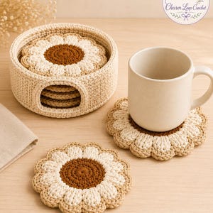 May include: A set of round, crocheted flower-shaped coasters in cream and brown, featuring a central brown circle surrounded by cream petals. The coasters are stored in a matching cylindrical crocheted holder, with one coaster placed under a plain mug.