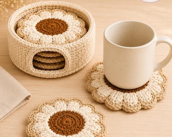 May include: A set of round, crocheted flower-shaped coasters in cream and brown, featuring a central brown circle surrounded by cream petals. The coasters are stored in a matching cylindrical crocheted holder, with one coaster placed under a plain mug.