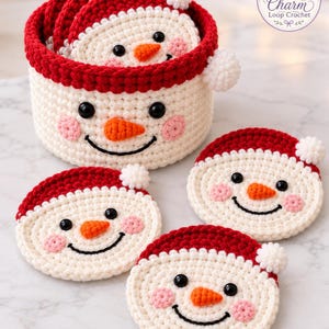 May include: A set of round, crocheted snowman coasters and a matching cylindrical storage basket. Each piece features a cream-colored face, a red hat with a white pom-pom, black button eyes, a small orange nose, and pink stitched cheeks.