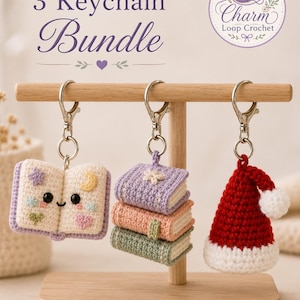 May include: A 3 Keychain Bundle featuring three crocheted items hanging from a wooden stand. The items include an open book with embroidered shapes, a stack of three small books in pastel colors, and a red and white crocheted Santa hat.