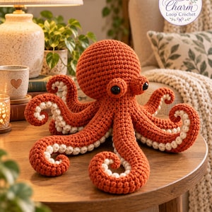 May include: A rust-colored crochet octopus plush toy featuring a large rounded head, two prominent black eyes, and eight curled tentacles with textured white undersides. The item includes a circular logo in the corner reading Charm Loop Crochet.