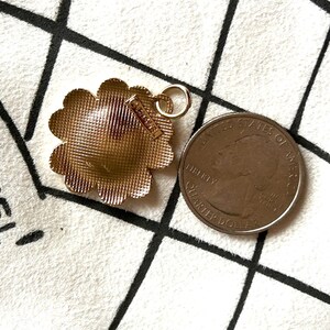 May include: Gold-toned flower-shaped pendant with a textured surface and a small tag that reads "CHANEL". The pendant has a loop for attaching to a chain. A US quarter is next to the pendant.