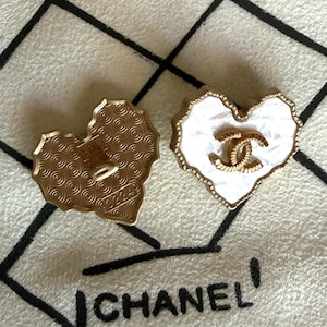 May include: Two heart-shaped buttons with gold-tone metal edges. One button displays a white marbled surface with a central gold-tone interlocking CC logo. The other button shows a gold-tone back with a repeating circular pattern and the text 92249.