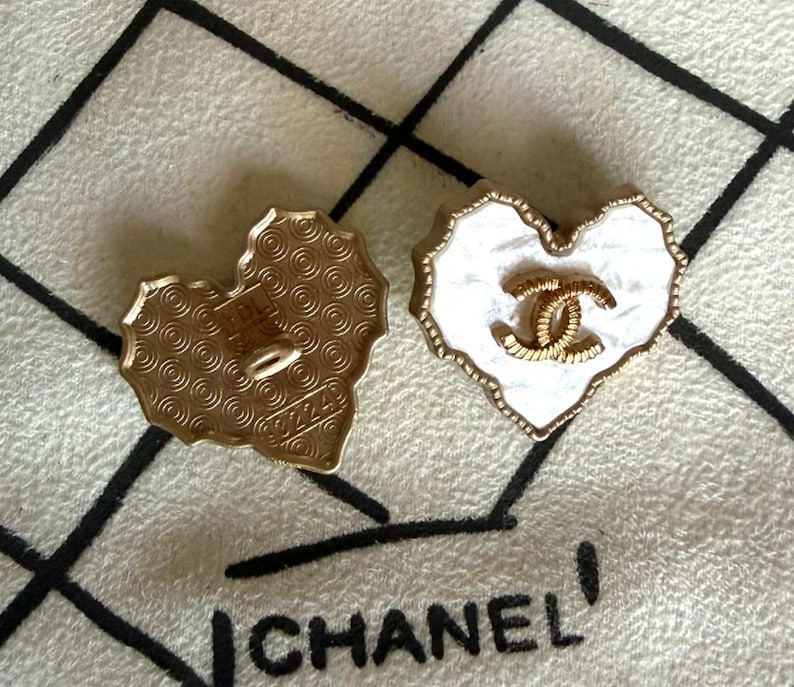 May include: Two heart-shaped buttons with gold-tone metal edges. One button displays a white marbled surface with a central gold-tone interlocking CC logo. The other button shows a gold-tone back with a repeating circular pattern and the text 92249.