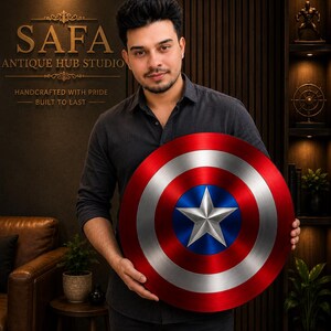 May include: A circular shield featuring a metallic finish with concentric rings in red, silver, and blue, centered with a prominent five-pointed silver star. The design mimics a classic superhero emblem with a brushed texture and vibrant colors.