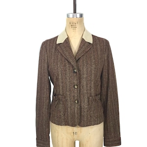 May include: A brown and cream striped blazer with a cream collar and gold buttons. The blazer has a fitted silhouette and pockets on the front.