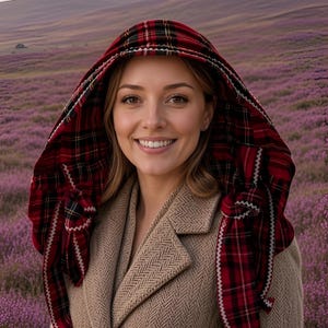 May include: A red and black tartan headscarf with a white zigzag stitched border draped over the head, worn with a tan herringbone coat featuring brown buttons. The headscarf is tied at the sides, framing the face with its classic plaid pattern.