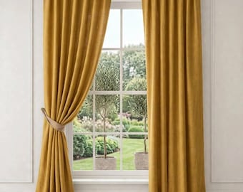 May include: A pair of floor-length mustard yellow curtains hanging from a silver rod. The left curtain is gathered and secured with a beige tieback, while the right curtain hangs straight down, framing a window with a view of a garden.