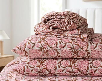 May include: A bedding set featuring a cream-colored base with a repeating floral pattern in shades of pink and brown. The set includes a folded fitted sheet, two rectangular pillowcases, and a flat sheet, all displaying the same botanical print.