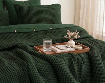 May include: A dark forest green waffle-weave duvet cover and matching pillowcases featuring a button-down closure. A wooden serving tray holds a clear glass of water, a small white ceramic vase with dried flowers, and a book.