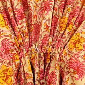 Puede incluir: Una prenda de tela de color amarillo claro con un patr&oacute;n repetitivo de motivos florales rosas y naranjas con detalles de enredaderas. El material est&aacute; fruncido en el centro con un cord&oacute;n blanco visible, creando pliegues.