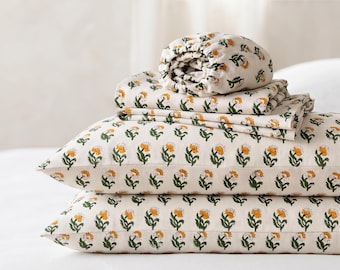 May include: A set of off-white bed linens featuring a repeating floral pattern of orange flowers with green stems and leaves. The set includes two rectangular pillowcases stacked at the bottom, a folded flat sheet, and a fitted sheet on top.