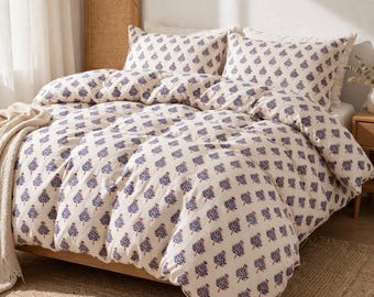 May include: A cream-colored duvet cover and two matching pillowcases featuring a repeating pattern of small, dark blue and reddish-brown tree motifs. A textured, off-white throw blanket is draped over the side of the bed.