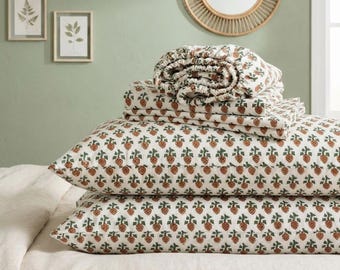 May include: A stack of bedding featuring a white background with a repeating pattern of small brown pinecones and green leaves. The set includes two rectangular pillowcases and a folded flat sheet, all made of a light-colored fabric.