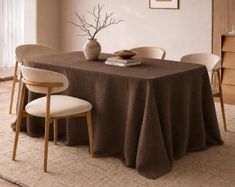 Puede incluir: Escena de comedor con un mantel rectangular marrón oscuro. Cuatro sillas con asientos color crema y marcos de madera rodean la mesa. Un jarrón con ramas y un cuenco están sobre la mesa.