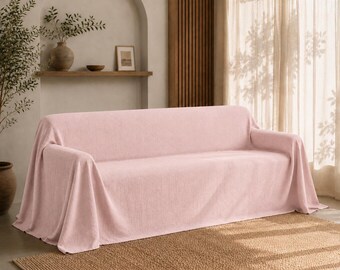 May include: A light pink sofa cover with a textured, woven fabric finish. The cover drapes over the entire sofa, including the backrest, seat, and armrests, creating a uniform, soft appearance that contours to the shape of the furniture piece.