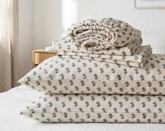 May include: A set of cream-colored bed linens featuring a repeating small blue floral print. The set includes two rectangular pillowcases stacked horizontally and a folded fitted sheet with elasticized edges resting on top.